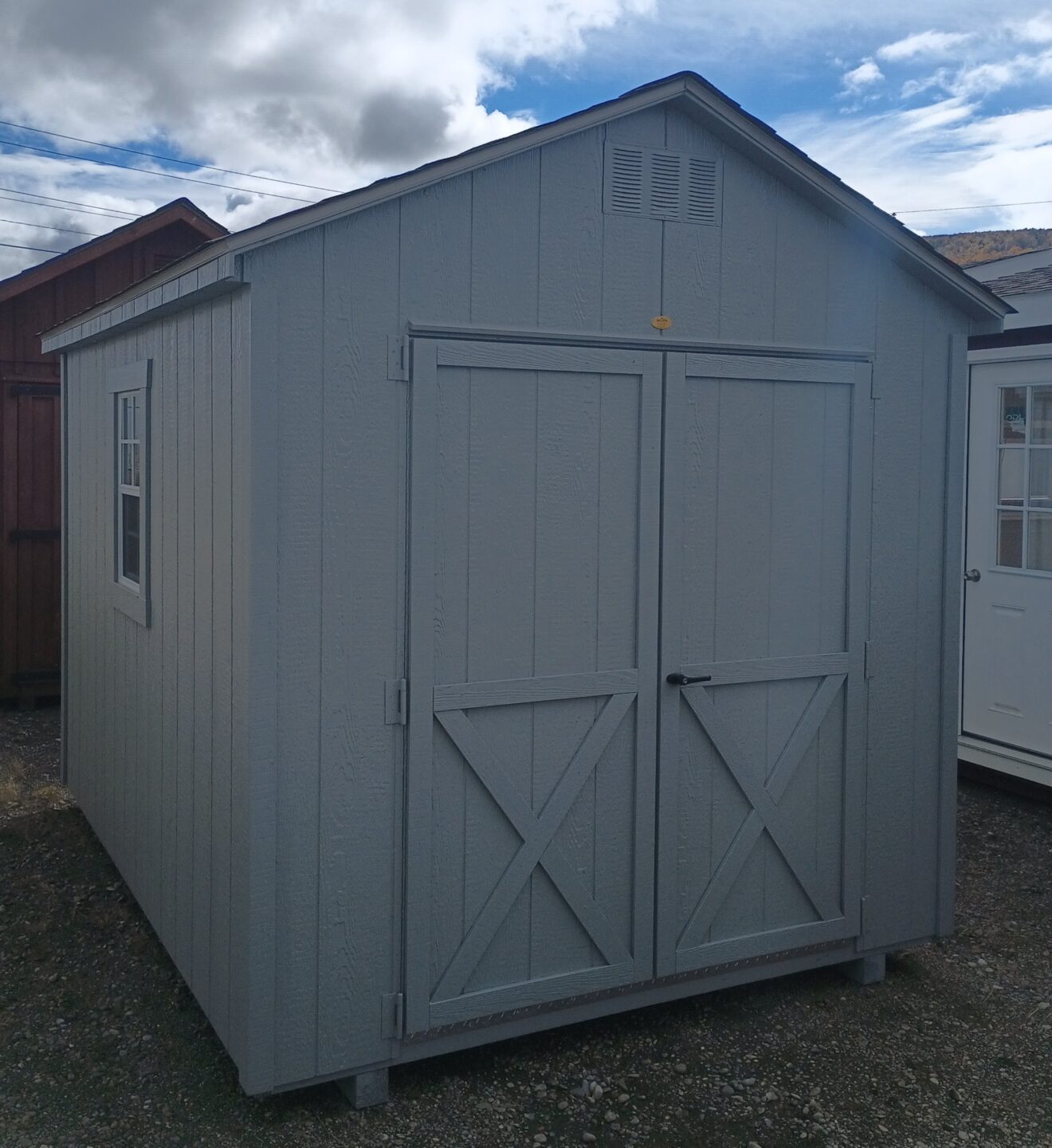 Small gray shed with peaked roof and double doors with shingled roof