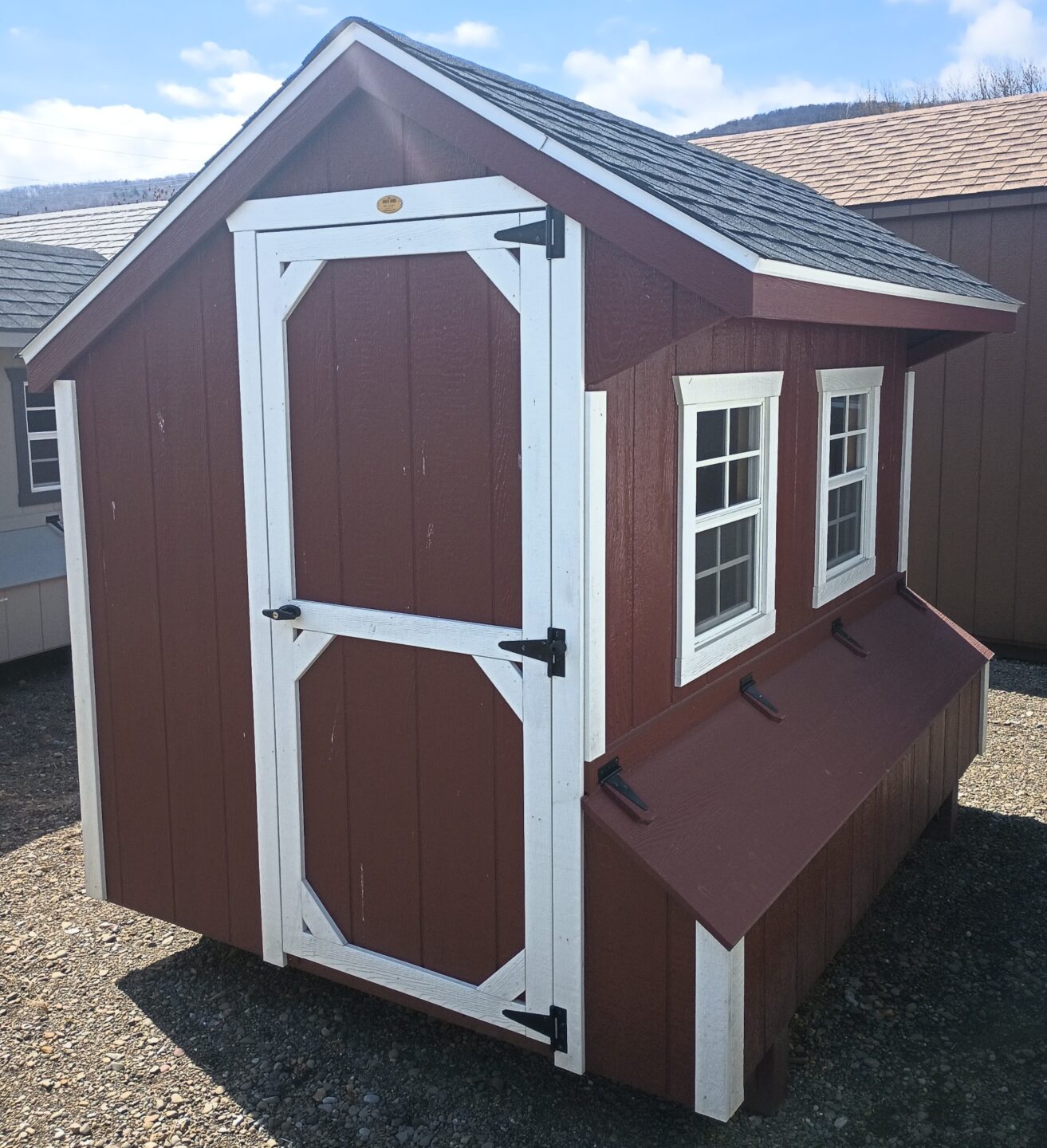 Red quaker style chicken coop with white trim, shingles an access door and 2 windows