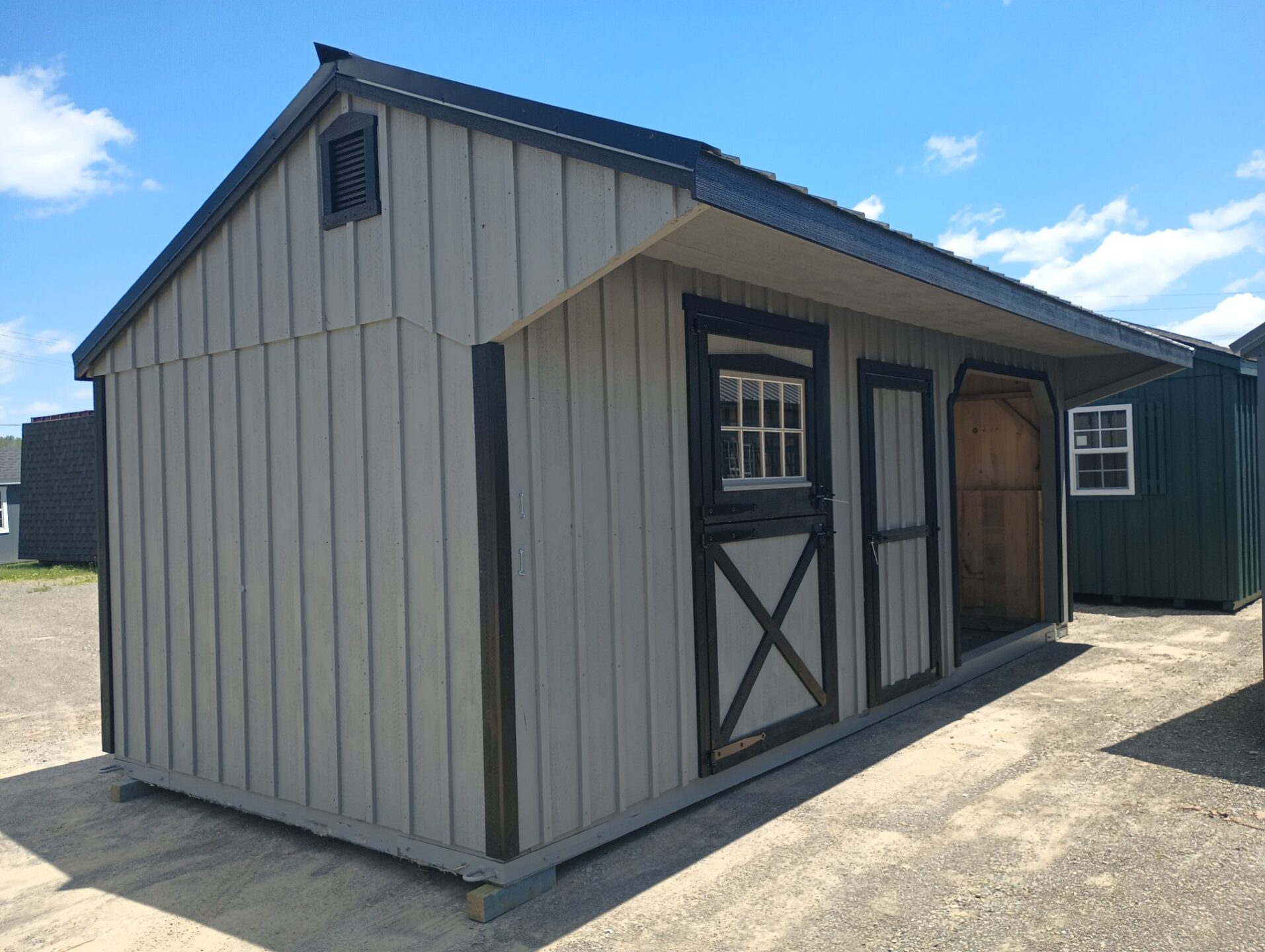 Large grey horse barn with black trim and overhang.  Includes stall at the end, center tack room and run in area at the end of the structure.