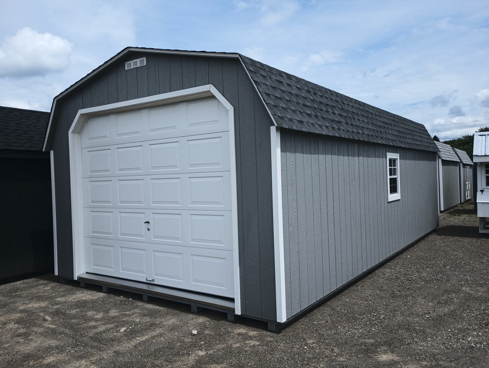 Large grey garage with white trim and white overhead door with no windows, shingled roof and a window on each side of the building