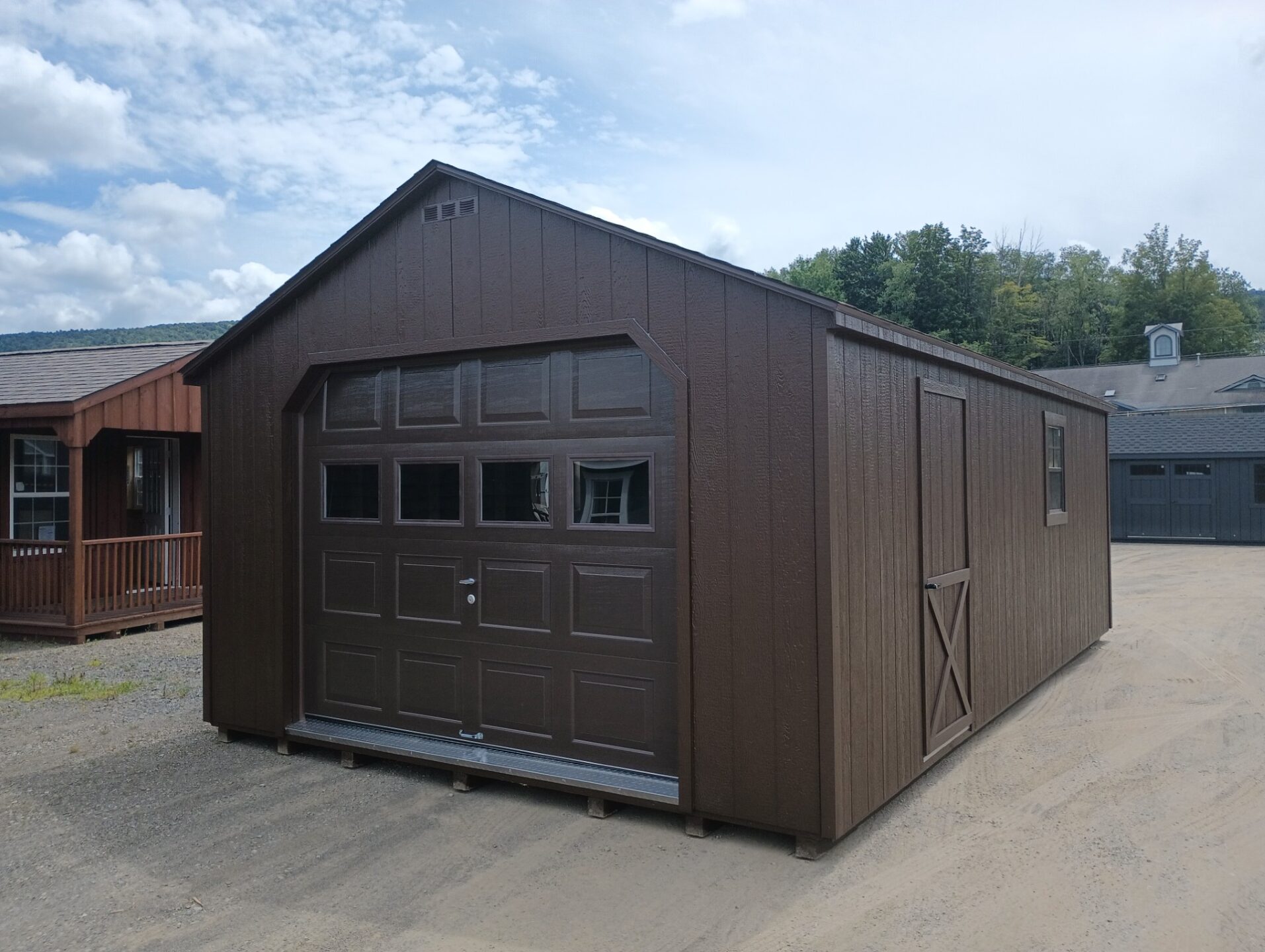 Large brown garage with overhead garage door, side door and windows with a shingled roof