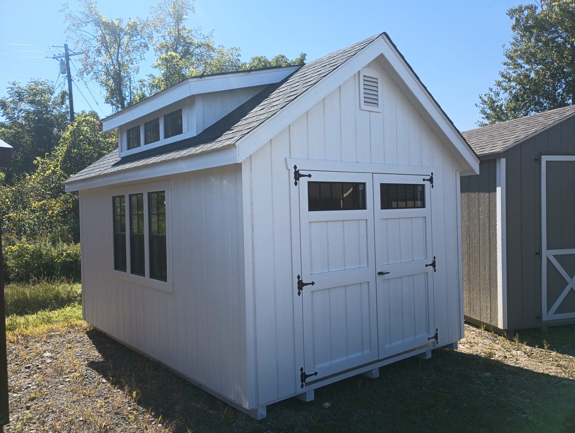 White shed with double doors with transom windows, triple transom dormer over three windows, window on back wall with workbench below