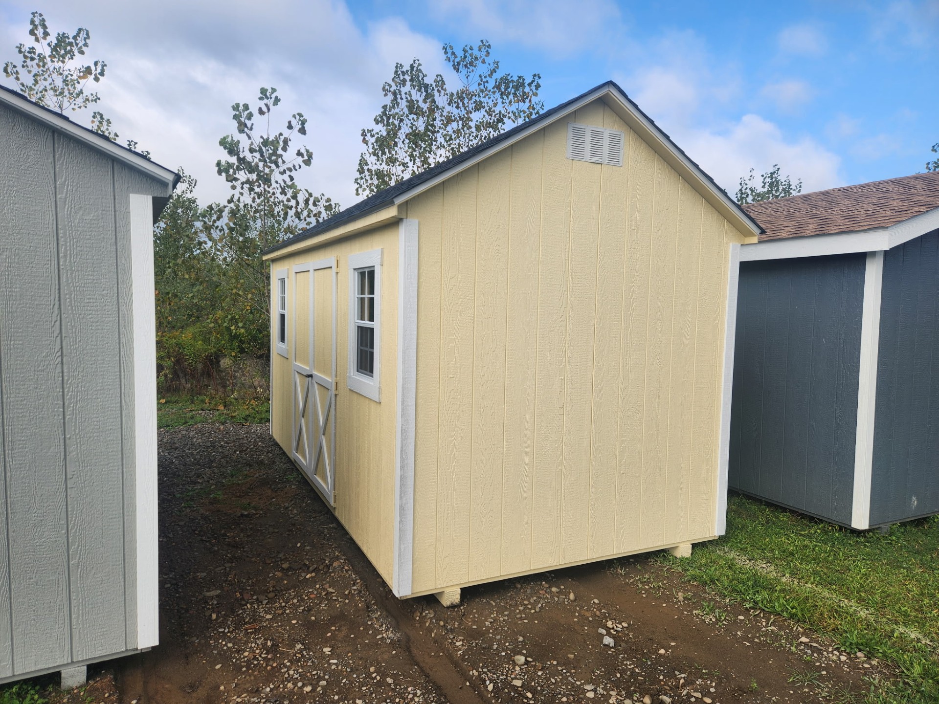 Cream color shed with double doors and two windows on front and shingled roof