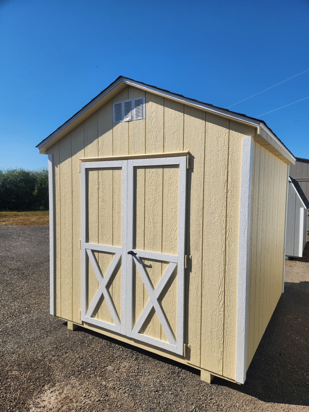 Small a frame style shed with cream siding, white trim, double doors, shingles on the roof and gable vents
